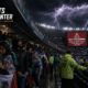 Soccer fans in rain ponchos take shelter at Estadio Azteca as a severe storm approaches before Mexico vs England at World Cup 2026.