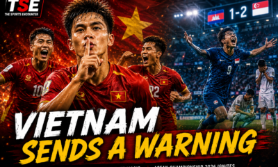Vietnam players celebrate their dominant opening-day victory over Timor-Leste during the 2026 ASEAN Championship, with Nguyen Dinh Bac leading the celebration in the foreground, while Singapore's Ilhan Fandi celebrates his dramatic late winner against Cambodia in the background. The official The Sports Encounter logo appears in the top-left corner beneath the headline, "Vietnam Sends a Warning."