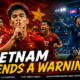 Vietnam players celebrate their dominant opening-day victory over Timor-Leste during the 2026 ASEAN Championship, with Nguyen Dinh Bac leading the celebration in the foreground, while Singapore's Ilhan Fandi celebrates his dramatic late winner against Cambodia in the background. The official The Sports Encounter logo appears in the top-left corner beneath the headline, "Vietnam Sends a Warning."