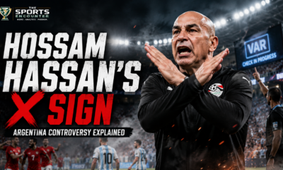 Hossam Hassan makes a crossed-arm X gesture during Egypt’s controversial World Cup match against Argentina, with VAR and refereeing tension highlighted in the background.