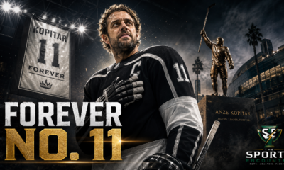 Anze Kopitar in a black No. 11 hockey uniform stands beneath arena lights beside a retired jersey banner and bronze statue, honoring his 20-season Los Angeles Kings career, two Stanley Cups and permanent franchise legacy.