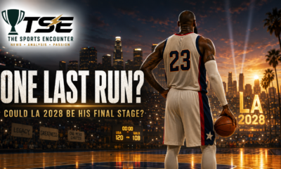A veteran basketball superstar wearing No. 23 stands with his back to the camera, holding a ball and looking across a glowing court toward the Los Angeles skyline and “LA 2028” lights.